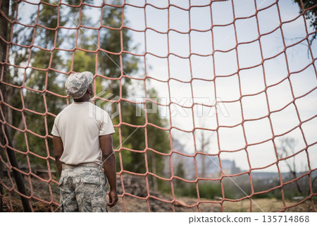 African American man in camouflage standing facing orange rope cargo net in forest training ground African American man in camouflage standing facing orange rope cargo net in forest training ground 135714868
