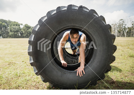 Male athlete crawling through large tractor tire on grassy field with obstacle course Male athlete crawling through large tractor tire on grassy field with obstacle course 135714877