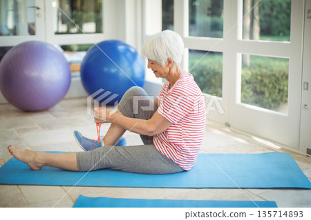 Senior woman stretching on blue exercise mat in home gym with stability balls, copy space 135714893