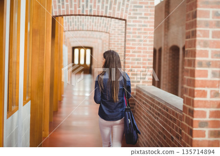 Female student walking through brick arch corridor with wooden windows carrying dark shoulder bag Female student walking through brick arch corridor with wooden windows carrying dark shoulder bag 135714894