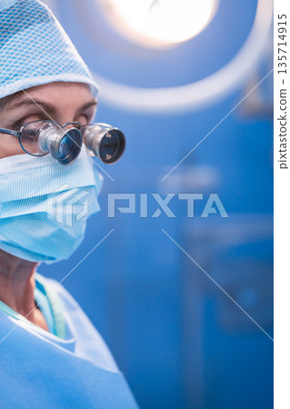 Senior male surgeon performing surgery under light wearing loupes in operating room, copy space Senior male surgeon performing surgery under light wearing loupes in operating room, copy space 135714915