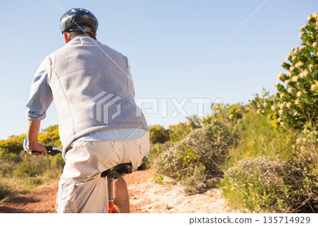 Mature male cyclist riding bicycle on trail through scrubland wearing helmet and vest, copy space Mature male cyclist riding bicycle on trail through scrubland wearing helmet and vest, copy space 135714929