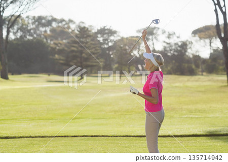 Woman golfer raising golf club overhead on fairway wearing sports visor and glove, copy space Woman golfer raising golf club overhead on fairway wearing sports visor and glove, copy space 135714942
