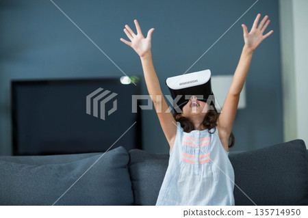 Female child raising arms exploring virtual reality headset on sofa in living room with TV screen Female child raising arms exploring virtual reality headset on sofa in living room with TV screen 135714950