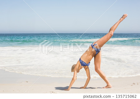 Woman cartwheeling in blue bikini on white sand beach at water's edge with waves, copy space Woman cartwheeling in blue bikini on white sand beach at water's edge with waves, copy space 135715062