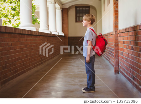 Boy waiting in school corridor with brick archways carrying red backpack, copy space 135715086