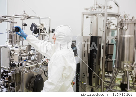 Mid-adult female technician in coverall operating valve wheel in sterile lab with pipes, copy space Mid-adult female technician in coverall operating valve wheel in sterile lab with pipes, copy space 135715105