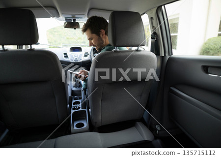Man leaning forward and checking smartphone in compact car near console cup holders, copy space 135715112