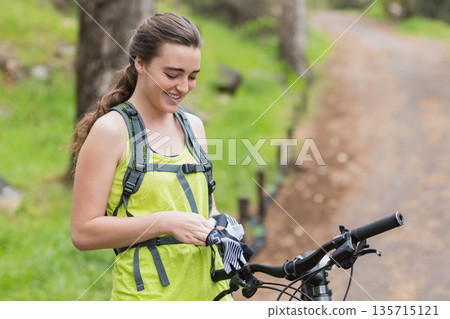 Woman wearing backpack standing next to bicycle on dirt trail adjusting striped gloves, copy space Woman wearing backpack standing next to bicycle on dirt trail adjusting striped gloves, copy space 135715121