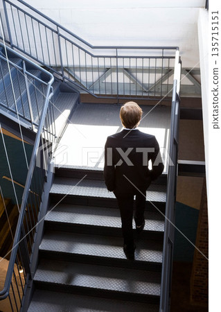 Business male ascending steel staircase with handrails in industrial stairwell lighting white walls 135715151