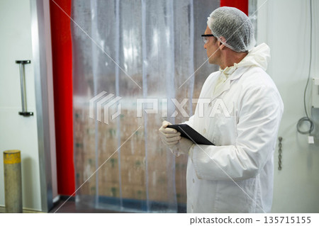 Man wearing protective attire checking tablet in hall near strip curtain, boxes cable, copy space 135715155