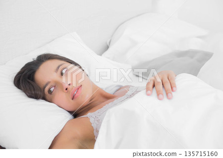 Woman reclining on bed wearing lace-trim camisole while gazing left atop white sheets and duvet Woman reclining on bed wearing lace-trim camisole while gazing left atop white sheets and duvet 135715160