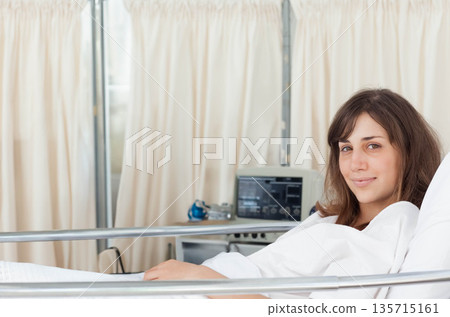 Woman patient reclining in hospital bed with metal rail beside vital signs monitor, copy space 135715161
