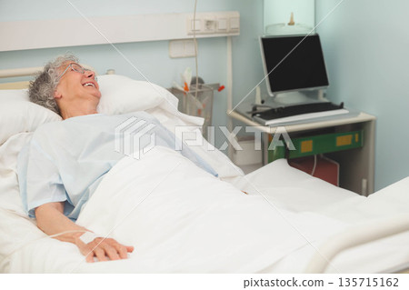 Senior woman resting on hospital bed with IV line and monitor on bedside table, copy space 135715162
