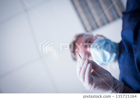 Mature adult dentist holding dental probe and wearing mask and gloves at clinic, copy space 135715164