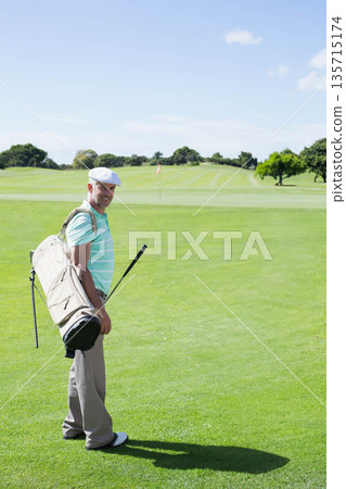Senior man smiling on golf course putting green while holding golf bag and club, copy space Senior man smiling on golf course putting green while holding golf bag and club, copy space 135715174