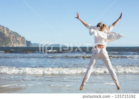 Jumping woman wearing white shirt and pants on sandy shoreline with waves and cliffs, copy space Jumping woman wearing white shirt and pants on sandy shoreline with waves and cliffs, copy space 135715192