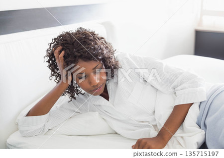 African American woman reclining on white bed in bedroom wearing pajama shirt and gray pants African American woman reclining on white bed in bedroom wearing pajama shirt and gray pants 135715197