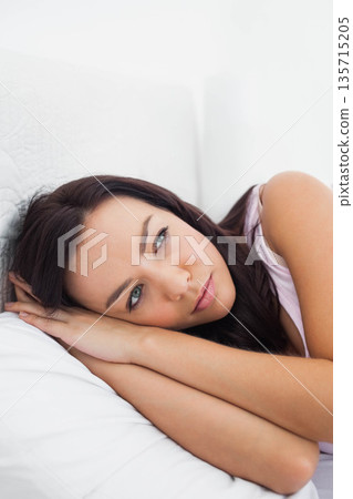 White adult woman lying on bed resting head on pillow in bedroom with white quilted bedding 135715205