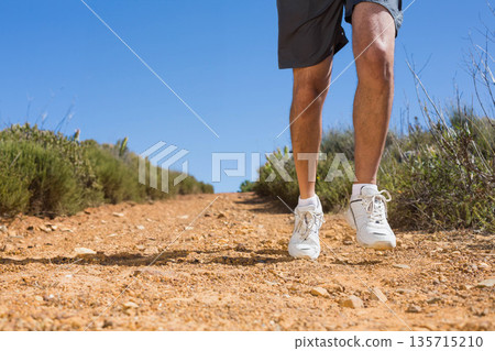 Male runner wearing gray shorts and white running shoes, jogging along dirt trail, copy space 135715210