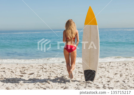 woman walking barefoot toward teal waves on beach beside surfboard with yellow tip, patterned base woman walking barefoot toward teal waves on beach beside surfboard with yellow tip, patterned base 135715217