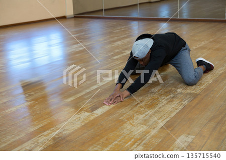 African American man in sportswear stretching forward on dance floor with mirror, copy space African American man in sportswear stretching forward on dance floor with mirror, copy space 135715540