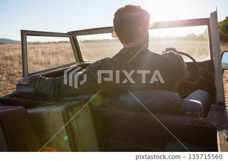 Mid adult man driving jeep gripping steering wheel along dirt path through grass at golden hour Mid adult man driving jeep gripping steering wheel along dirt path through grass at golden hour 135715560