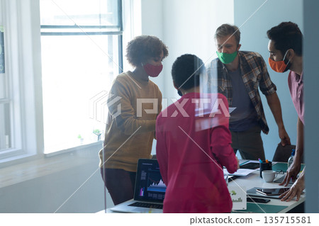 Diverse coworkers leaning around conference table at office discussing chart graphics on laptop 135715581