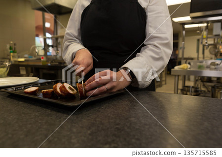 Female chef slicing roulade with knife on metal baking tray in professional kitchen Female chef slicing roulade with knife on metal baking tray in professional kitchen 135715585