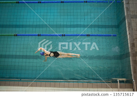 Female swimmer in swimsuit gliding in lap pool, performing front crawl over lane lines and ladder Female swimmer in swimsuit gliding in lap pool, performing front crawl over lane lines and ladder 135715617