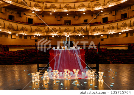 Romantic "MARRY ME" proposal setup with glowing letters and candlelit table in grand theater auditorium 135715764