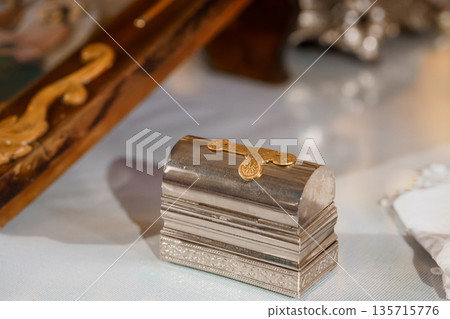 Ornate Silver Reliquary Box with Gold Clasp Displayed on White Cloth Near Religious Artifacts Ornate Silver Reliquary Box with Gold Clasp Displayed on White Cloth Near Religious Artifacts 135715776