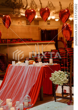 Romantic Red Heart Balloons and White Roses Table Setup in Elegant Theater Hall with Candles and Luxury Decor Romantic Red Heart Balloons and White Roses Table Setup in Elegant Theater Hall with Candles and Luxury Decor 135715802