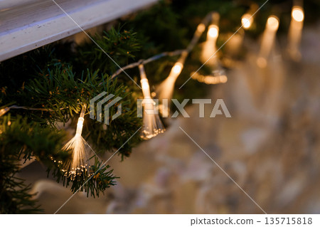 Warm Glowing Fiber Optic Lights Adorning Green Christmas Tree Branches in Cozy Holiday Decor Setting 135715818