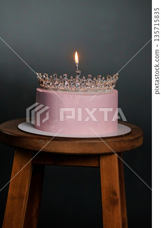 Elegant Pink Birthday Cake with Sparkling Crown Tiara and Single Lit Candle on Wooden Stool Elegant Pink Birthday Cake with Sparkling Crown Tiara and Single Lit Candle on Wooden Stool 135715835