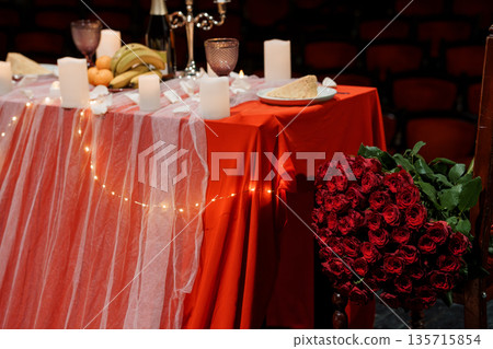 Romantic Red Table Setting with Rose Bouquet, Candles, and Fruit Arrangement in Theater Venue 135715854