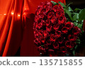Vibrant Bouquet of Red Roses with Green Leaves Against Warm Orange Curtains and Fairy Lights 135715855