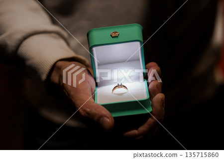 Elegant Engagement Ring in Green Box Held by Hands with Soft Lighting and Warm Background Elegant Engagement Ring in Green Box Held by Hands with Soft Lighting and Warm Background 135715860