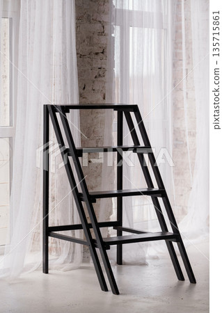 Modern Black Metal Ladder Stool in Minimalist Loft Interior with White Curtains and Exposed Brick Wall Modern Black Metal Ladder Stool in Minimalist Loft Interior with White Curtains and Exposed Brick Wall 135715861