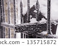 Snow-covered black iron fence with frosty textures and winter landscape backdrop in cold weather scene 135715872