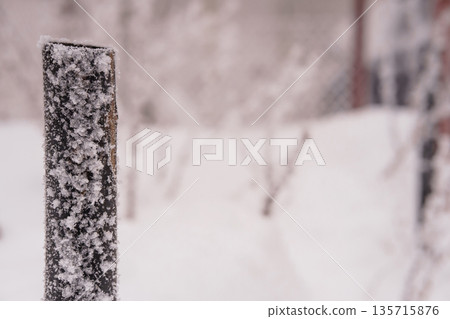Frost-covered wooden post in snowy winter landscape with blurred trees and serene white surroundings Frost-covered wooden post in snowy winter landscape with blurred trees and serene white surroundings 135715876