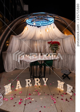 Romantic Proposal Setup Under Glass Dome with Red Roses, Candlelight, and "MARRY ME" Sign on Floor Romantic Proposal Setup Under Glass Dome with Red Roses, Candlelight, and "MARRY ME" Sign on Floor 135715880