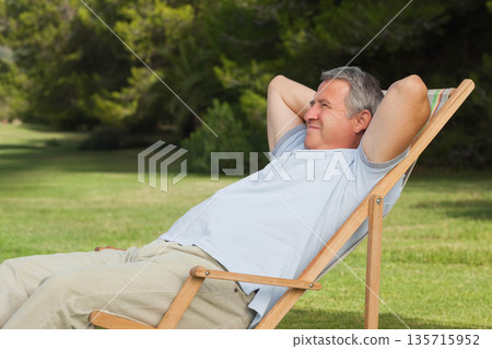 Mature man reclining in striped folding deck chair on lawn, wearing light-blue shirt, copy space Mature man reclining in striped folding deck chair on lawn, wearing light-blue shirt, copy space 135715952