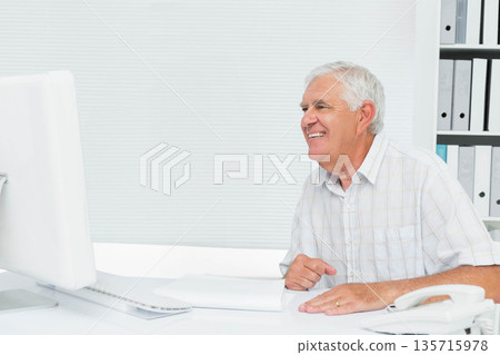 Senior male sitting at bright office on right, using desktop monitor, in checked shirt, copy space 135715978