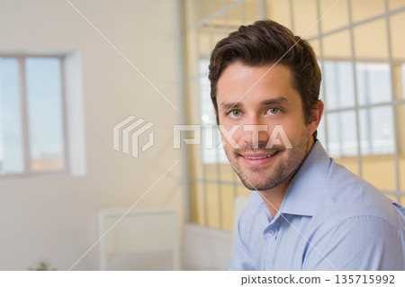 Man sitting at office in blue button-down shirt by large window with glass partition and plant 135715992