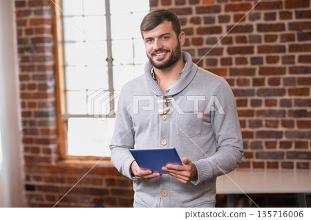 African American man standing by mullioned window in loft holding blue tablet, wearing gray sweater African American man standing by mullioned window in loft holding blue tablet, wearing gray sweater 135716006