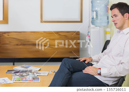 Man sitting on chair in waiting area, wearing button-down and jeans, wristwatch visible, copy space Man sitting on chair in waiting area, wearing button-down and jeans, wristwatch visible, copy space 135716011