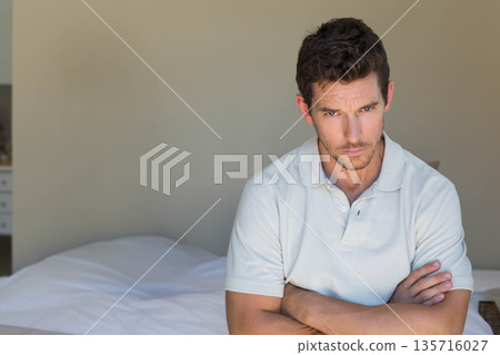 Man sitting on bed edge in bedroom wearing light polo, crossing arms, copy space Man sitting on bed edge in bedroom wearing light polo, crossing arms, copy space 135716027