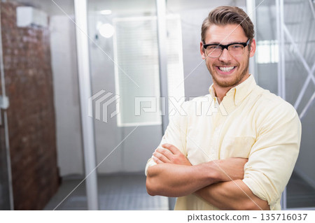 Man standing smiling arms crossed in office wearing glasses and yellow button-up shirt, copy space 135716037