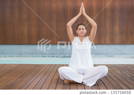 Adult woman meditating, hands joined overhead, sitting on deck in white clothes barefoot by pool Adult woman meditating, hands joined overhead, sitting on deck in white clothes barefoot by pool 135716038